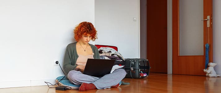 Student sat on the floor on a laptop with suitcase